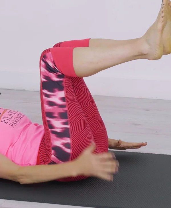 Woman, pink t-shirt, red leggings, exercising on mat.