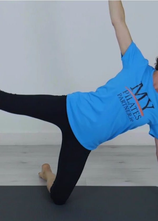 Woman, blue t-shirt, doing Pilates exercise on a grey mat